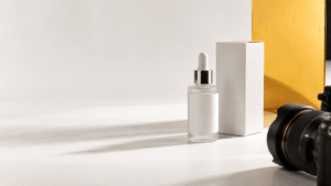 A skincare bottle and packaging arranged beside a camera lens on a clean studio surface, ready for a product photo shoot.